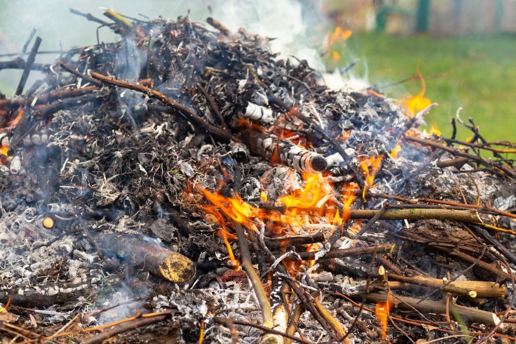 A large pile of burning branches and leaves with smoke.